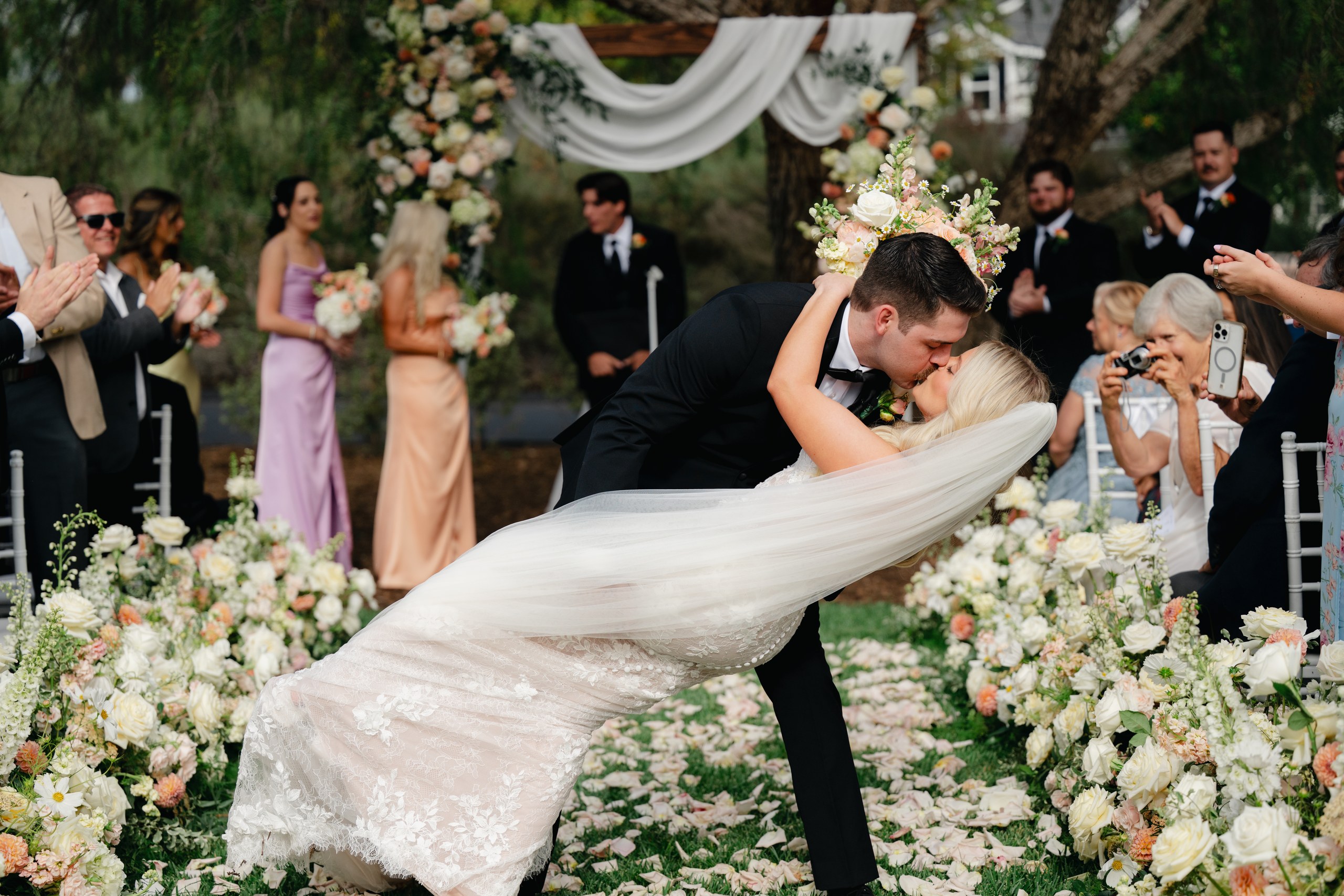 Groom dips the bride for a kiss at the end of their Olivenhain backyard wedding ceremony as guests cheer