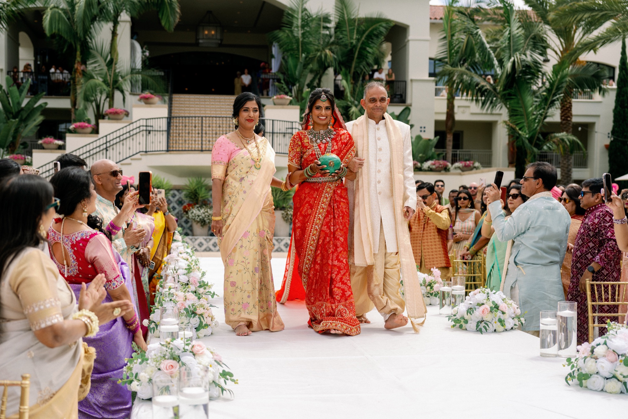 Indian bride in red saree walking down the aisle with her parents at Park Hyatt Aviara